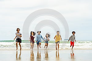 Group of children sister brother run and play happily together on the beach during the summer while visiting with family or school