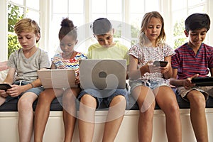 Group Of Children Sit On Window Seat And Use Technology