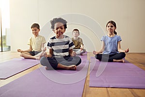 Group Of Children Sitting On Exercise Mats And Meditating In Yoga Studio