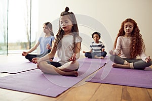 Group Of Children Sitting On Exercise Mats And Meditating In Yoga Studio photo