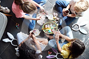 Group Of Children Sitting On Floor At Home Eating Chocolate Eggs They Have Found On Easter Egg Hunt