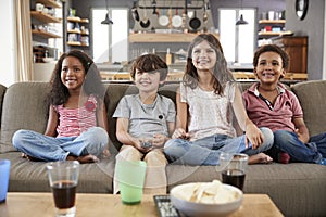 Group Of Children Sitting On Sofa Watching Television Together