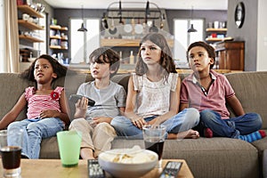 Group Of Children Sitting On Sofa Watching Television Together