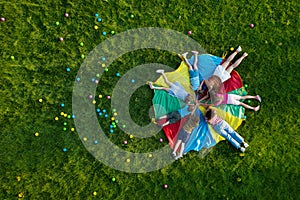 Group of children with teachers holding hands on rainbow playground parachute in park, top view. Summer camp activity