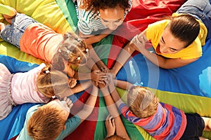 Group of children with teachers holding hands together on rainbow playground parachute, top view. Summer camp activity