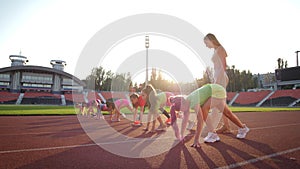 A group of children, on the treadmill at the stadium on a bright sunny day, warm up with the coach before the