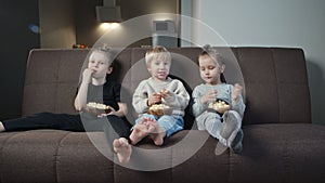 Group of children watching movie on TV in the evening at home and eat popcorn.