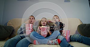 Group of children watching movie on TV in the evening at home and eat popcorn. V3