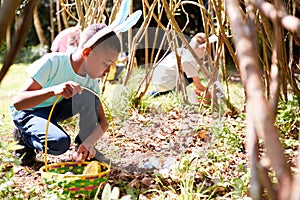 Group Of Children Wearing Bunny Ears Finding Easter Eggs Hidden In Garden