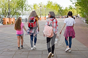 Group of children and women walking in the park. Urban background, river, sky. Back view.