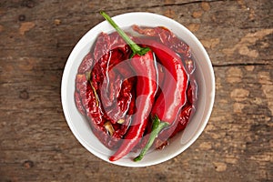 Group of chilli peppers and dried chilli inside white bowl on wooden table