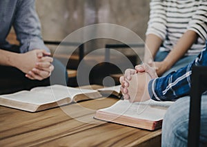 group of christian sitting around wooden table with open blurred bible page and praying to God together