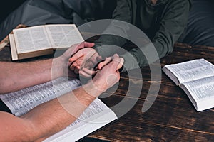 A group of Christians pray holding hands. On the table. The Holy Bible is open. Praying