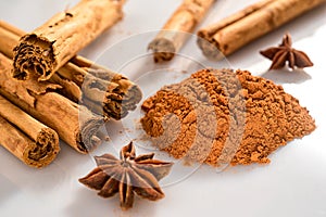 Group of cinnamon sticks with star anice and powder on a white and lucid backround photo