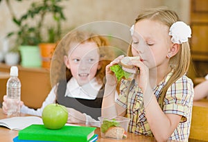 Group of classmates having lunch during break with focus on smiling girl with sandwich