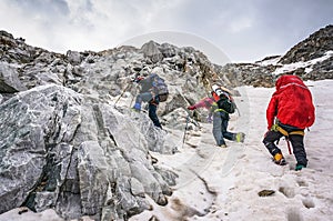 Group of climbers ascent to the mountain on a complex slope is composed of rock and snow