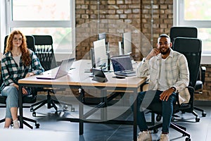 Group of colleagues, a woman with vibrant orange hair and a young African American businessman, sitting in a modern