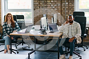 Group of colleagues, a woman with vibrant orange hair and a young African American businessman, sitting in a modern