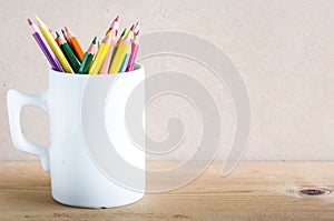 A group of color pencils in a white cup on wood