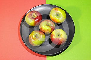 Group of colorful apples fruits on a black plate. Colored background. Top view.