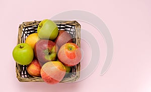 Group of colorful apples in a small wicker basket isolated on pink background