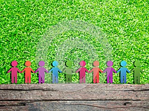 Group of colorful children figure icon standing on wooden timber and green grass meadow field. They holding hands together.