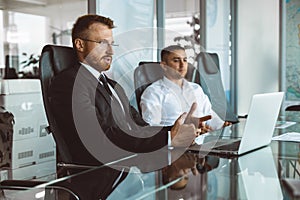 A group of company employees sits at a table in a meeting room. A team of young businessmen working and communicating