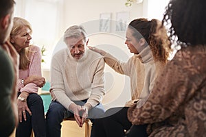 Group Consoling Man Speaking At Support Group Meeting For Mental Health Or Dependency Issues