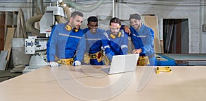 Group of construction workers engrossed in laptop data in an industrial factory, surrounded by machinery, amidst a clatter of photo