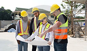 Group of construction workers gathered at a construction site reviewing some plan. Unfinished building, piles of construction