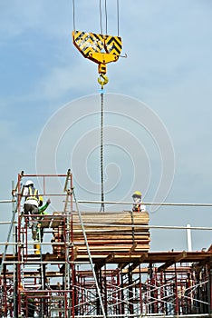 Group of construction workers lifting bundle of timber using mobile crane