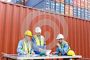 Group of container operators wearing helmets and safety vests meeting about logistics operations in container yards. Colleagues