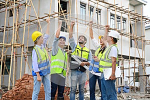 Group of contractors, engineers and formats in safety vests with helmets hands up to work together to successfully complete a