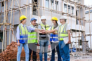 Group of contractors, engineers and formats in safety vests with helmets join hands to work together to successfully complete a