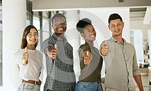 Group of creative colleagues smiling and gesturing thumbs up in creative office. Diverse business team standing together