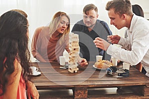 Group of creative friends sitting at wooden table. People having fun while playing board game