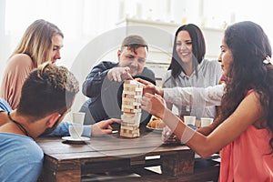 Group of creative friends sitting at wooden table. People having fun while playing board game