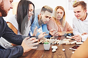 Group of creative friends sitting at wooden table. People having fun while playing board game