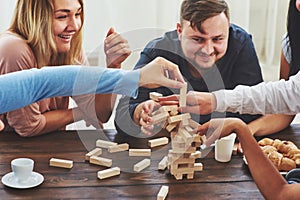 Group of creative friends sitting at wooden table. People having fun while playing board game