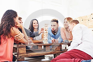 Group of creative friends sitting at wooden table. People having fun while playing board game