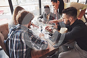 Group of creative friends sitting at wooden table. People having fun while playing board game