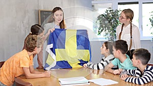 Group of curious preteen learners and young female teacher with flag of Sweden in classroom of academy