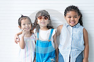 Group of cute Asian Caucasian and African little girls friends hug each other, smiling, posing in studio white background.