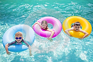 Group of cute kids playing on inflatable tubes in a swimming pool on a sunny day