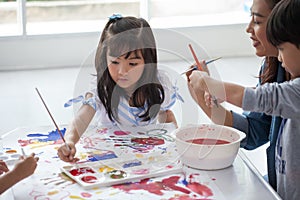 group of Cute little girl student painting  together with nursery teacher in classroom school . Happy children in a kindergarten