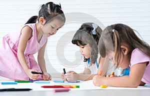 Group of cute little kids girls have fun drawing on paper while sitting and lying on the floor. Adorable happy diversity children