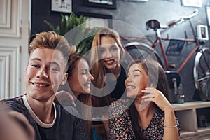 Group of cute teenagers taking selfie with cellphone while sitting in a restaurant with interior in retro style