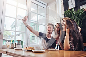 Group of cute teenagers taking selfie with cellphone while sitting in a restaurant with interior in retro style