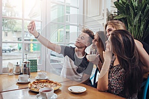 Group of cute teenagers taking selfie with cellphone while sitting in a restaurant with interior in retro style