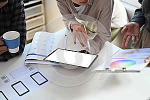 Group of designers in casual clothes working together with digital tablet and color calibration on table.
